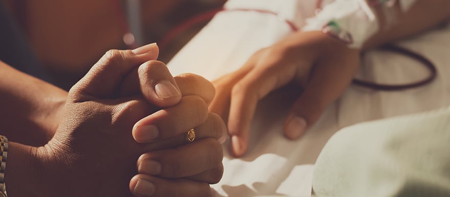 Person praying next to hospital bed